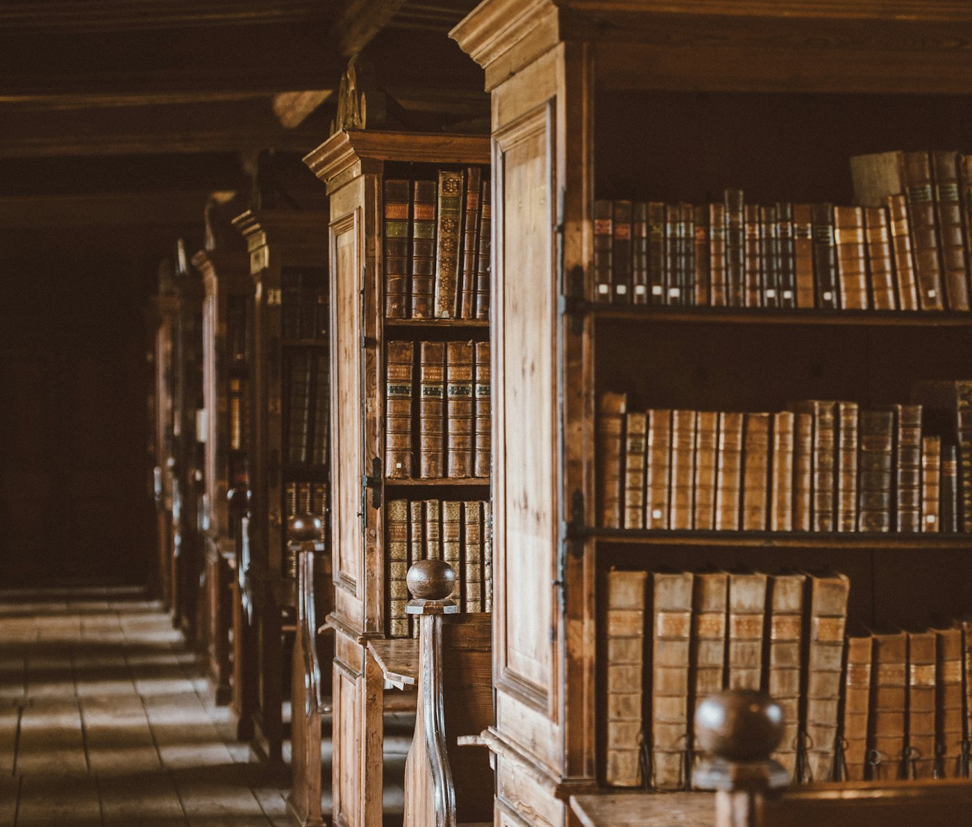 Deretan rak kayu berisi buku-buku tua di perpustakaan dengan cahaya hangat.